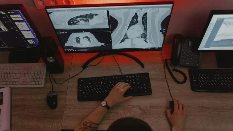 A radiologist reviews x-ray scans on multiple monitors at a desk, focusing on medical diagnostics.