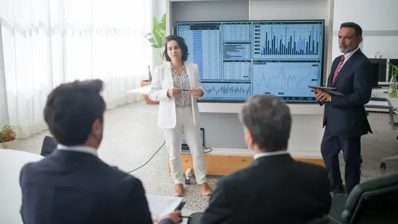 Colegas discutiendo gráficos financieros durante una reunión corporativa en una oficina moderna.