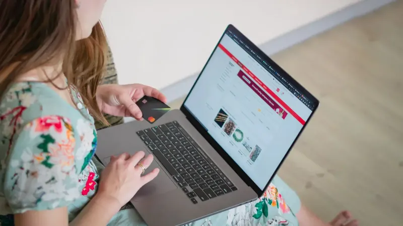 Woman in floral dress shopping online with a laptop and credit card indoors.