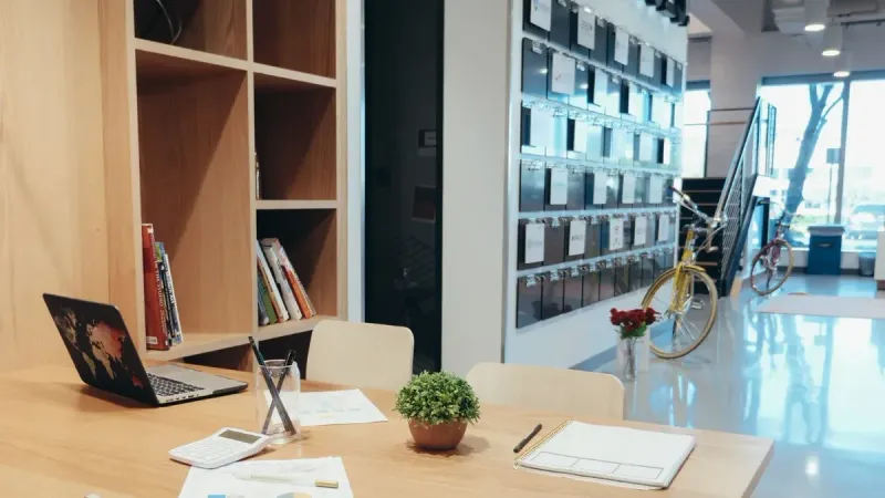 A modern office workspace featuring a laptop, documents, and a potted plant on a wooden table.