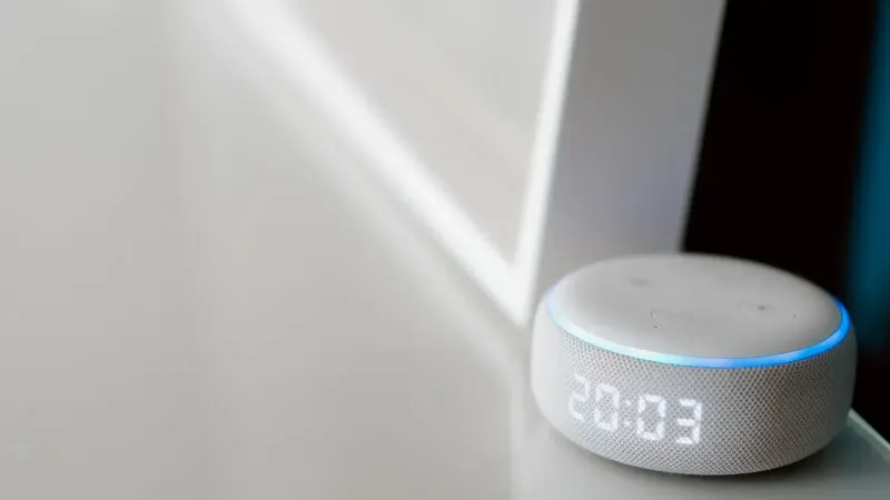 Close-up of a smart speaker with a digital clock display on a minimalist surface.