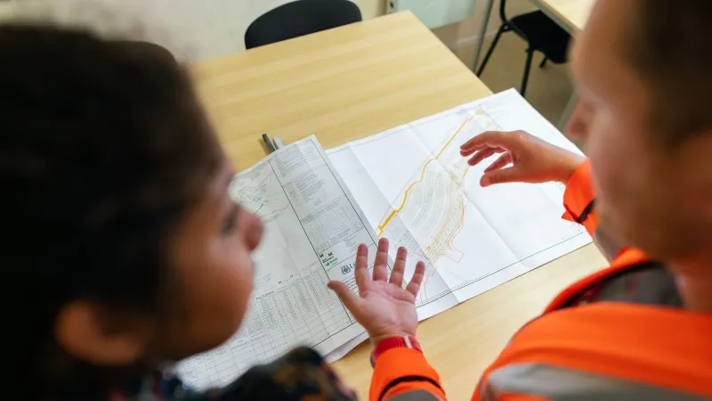 Two engineers reviewing construction blueprints on a table in an office setting.
