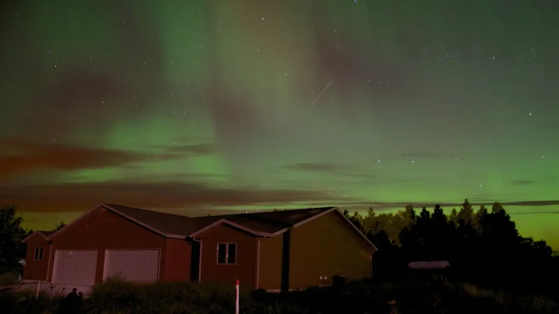 Scenic view of Northern Lights illuminating a house surrounded by nature at night.