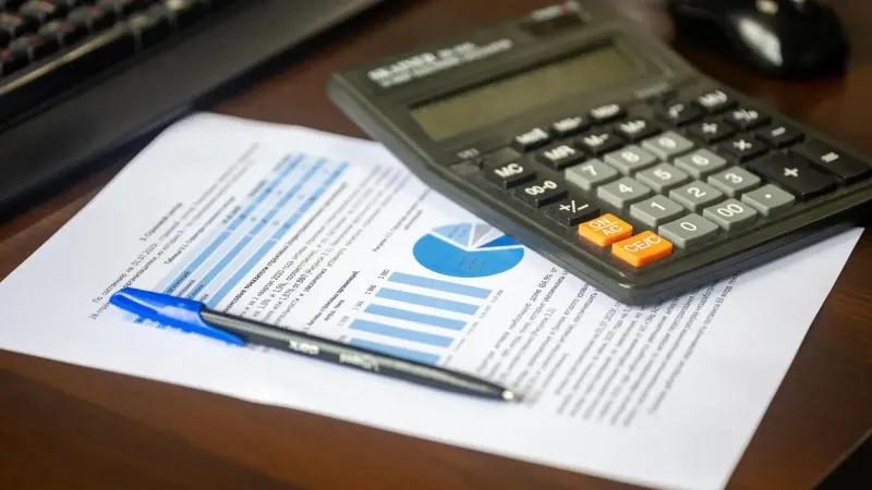 Desk with calculator, financial report, and pen, suggesting business analysis.