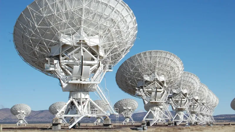 Array of radio telescopes at the Very Large Array in New Mexico under a clear blue sky.