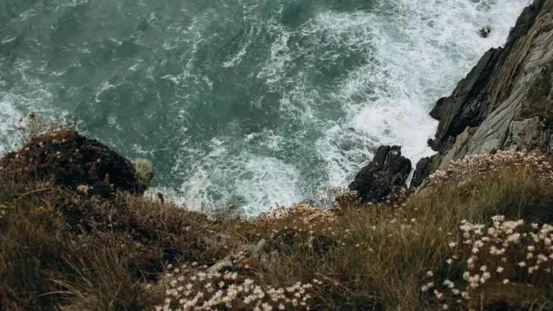 Vista desde un acantilado de olas turbulentas del océano contra la costa rocosa, mostrando la belleza de la naturaleza cruda.