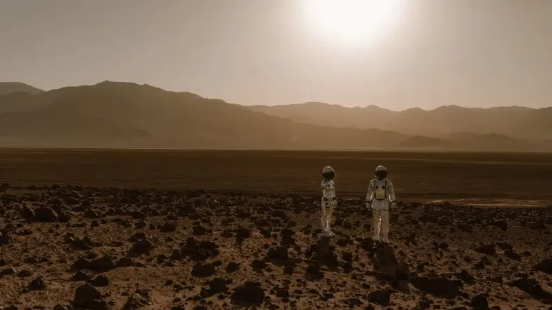 Astronauts in space suits explore a rocky, desert-like terrain resembling Mars at sunset.