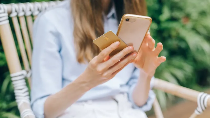 A woman making an online purchase using a smartphone and credit card outdoors.