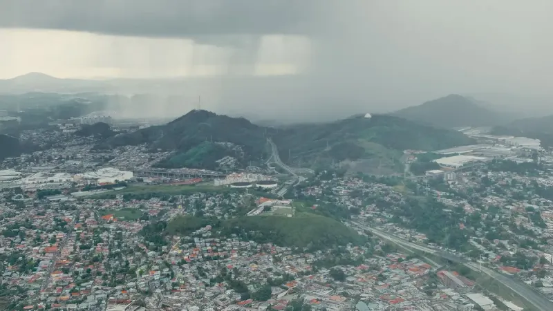 Aerial shot capturing a rainstorm approaching a sprawling urban landscape near hills.