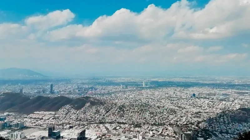 Stunning aerial view of Monterrey's cityscape with mountains and clouds against a blue sky.