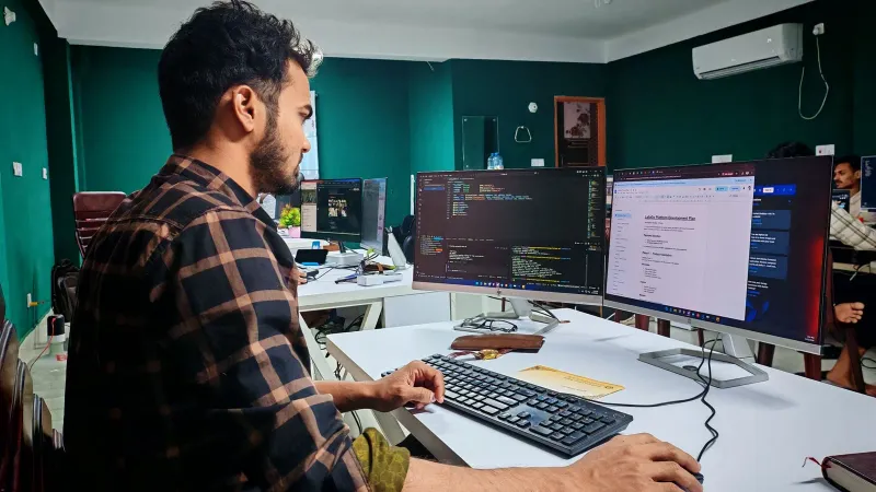 Software developer coding on dual monitors in a well-lit modern office, focused and engaged.