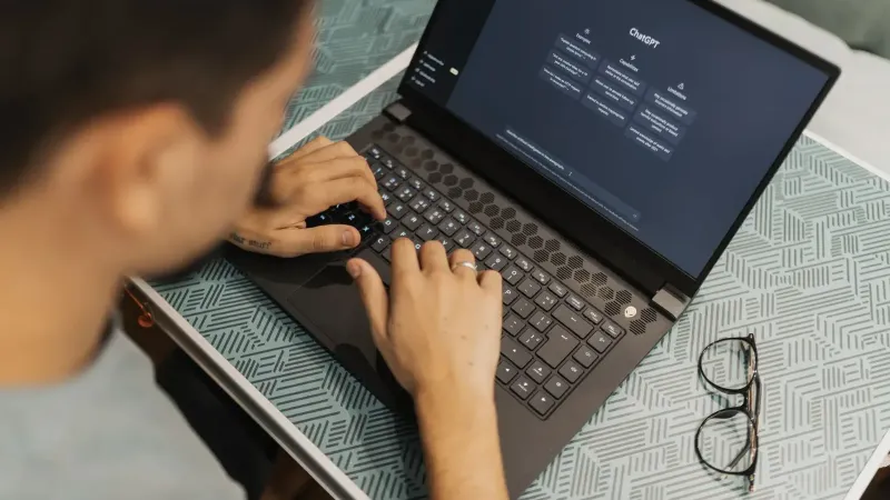 A man working on a laptop with AI software open on the screen, wearing eyeglasses.
