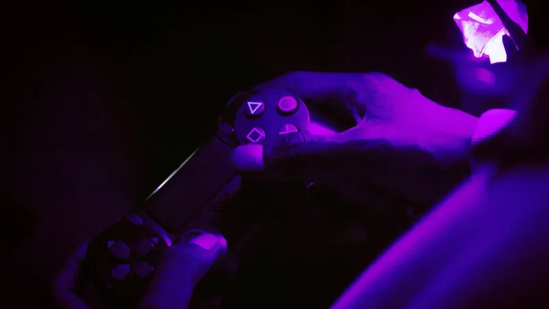 A close-up shot of hands gripping a gaming controller, illuminated by purple light, creating a vibrant atmosphere.