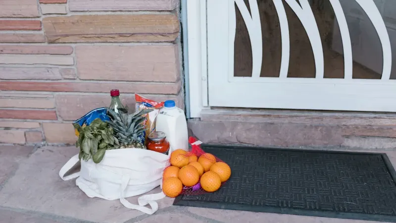 Reusable bag with groceries and fruits left at doorstep, highlighting delivery service.