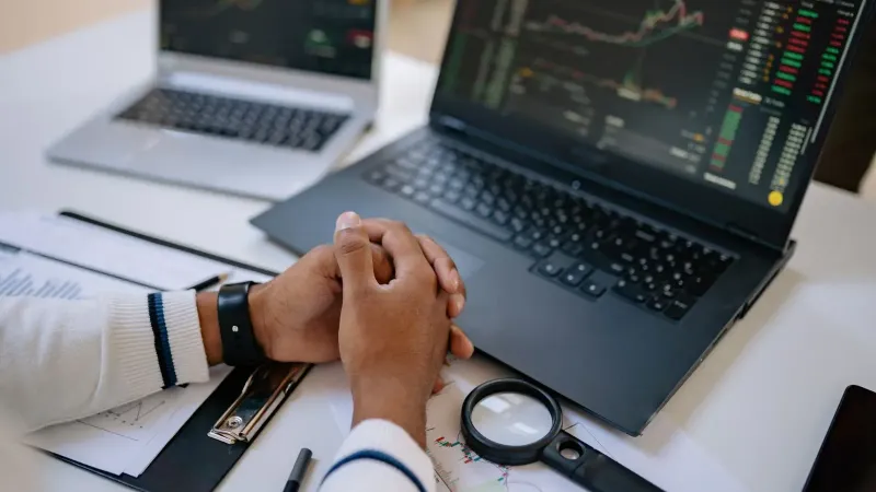 Man seated at a desk using laptops to monitor stock market trends and investments.