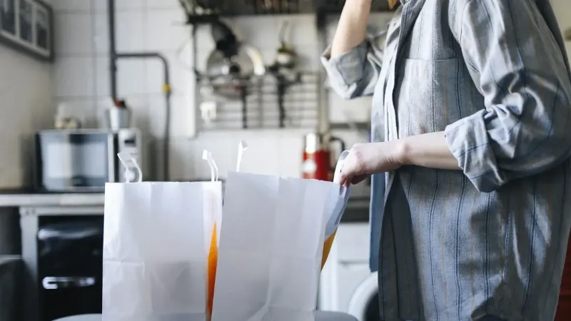 Woman in casual attire handling paper bags for delivery service in a kitchen setting.
