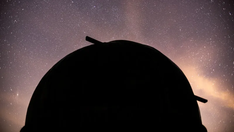 Silhouette of an observatory dome against a dramatic starry night sky.