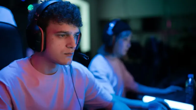 Man with headset engaged in intense gaming session under neon lights.