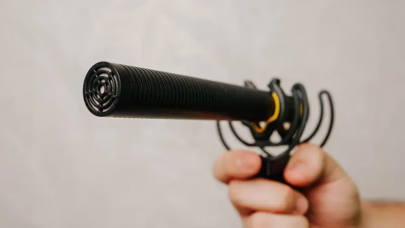 Mano sosteniendo un micrófono de escopeta con cubierta de espuma, ideal para grabación de voz y captura de audio.