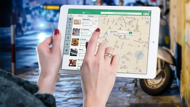 Hands using a digital map on a tablet in an urban setting at night, illustrating navigation and technology.
