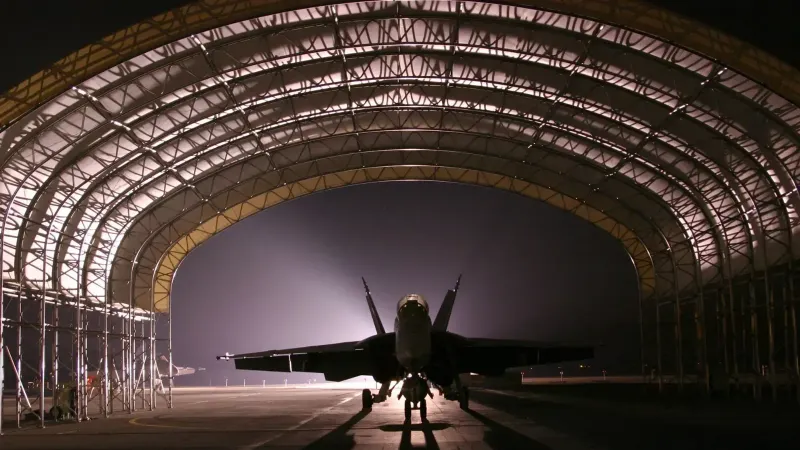 Silhouetted fighter jet in an illuminated hangar at night creates a dramatic scene.
