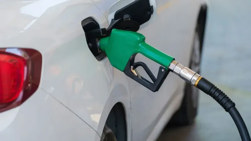 Close-up de una boquilla verde repostando un coche blanco en una gasolinera.