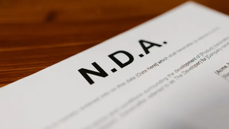 Primer plano enfocado de un documento NDA en un escritorio de madera, destacando los detalles del contrato.