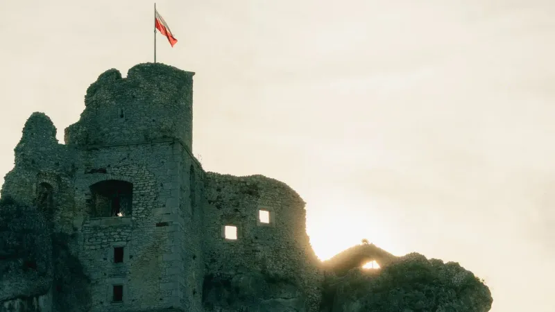 Scenic view of Ogrodzieniec Castle silhouetted against the sunrise, featuring a Polish flag.