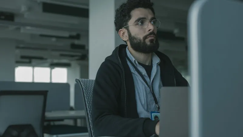 Man with eyeglasses working at a desk in an office setting, focused and engaged.