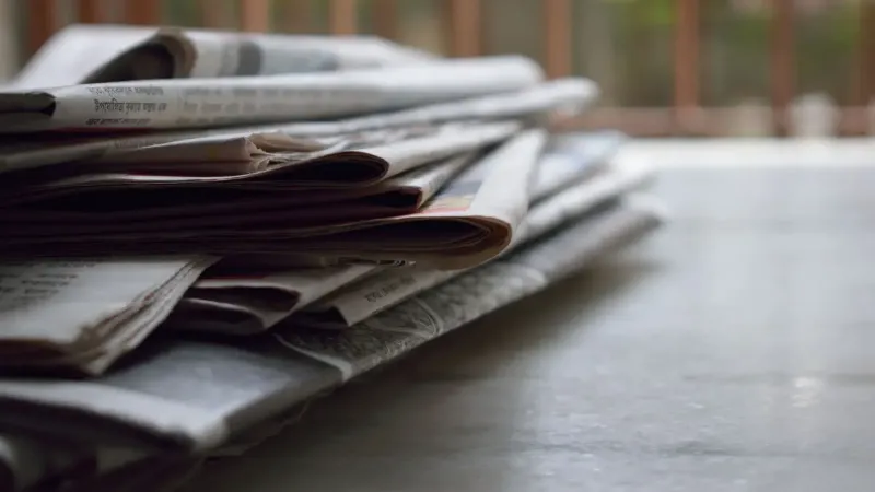 A close-up of a stack of newspapers resting on a desk, symbolizing information and media.