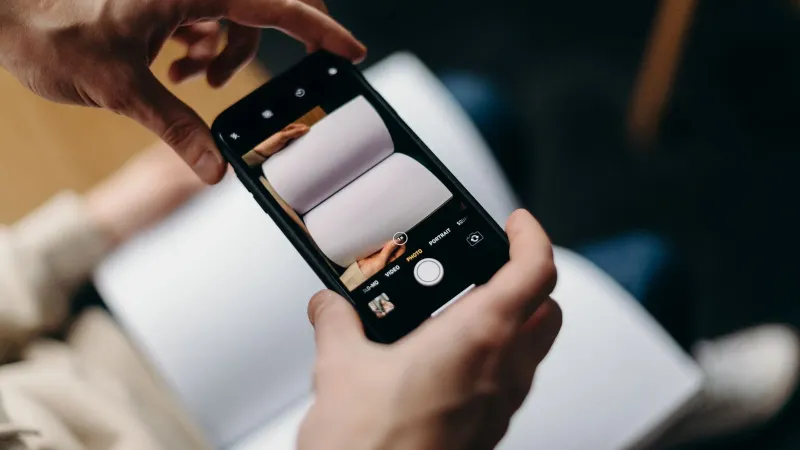 Person using smartphone to photograph blank open book. Concept of mobile photography and creativity.