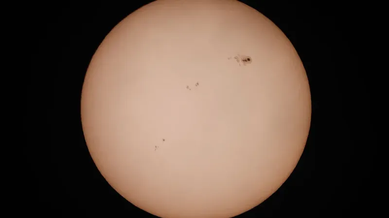 A detailed photograph of the sun highlighting visible sunspots against a dark background.