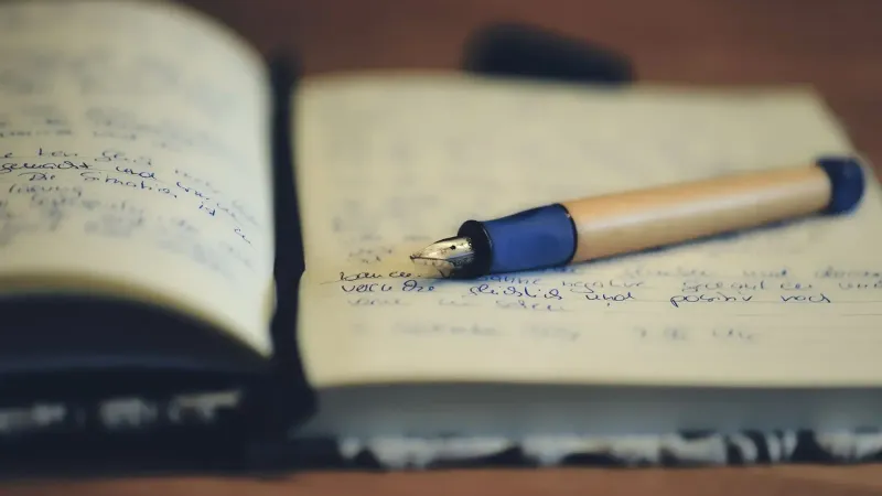A close up of a fountain pen resting on an open notebook, highlighting handwriting and the writing process.