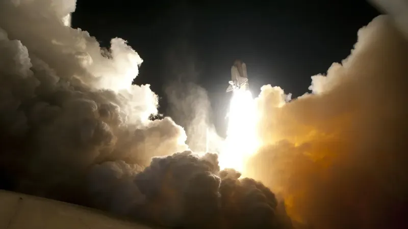 A dramatic image of a space shuttle launching into the night sky, surrounded by billowing smoke and intense light.