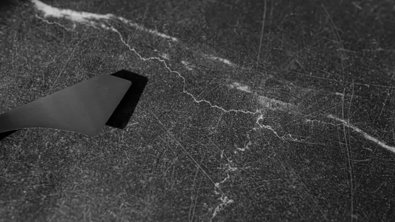 Black and white close-up of a scraper on a textured surface, highlighting details.