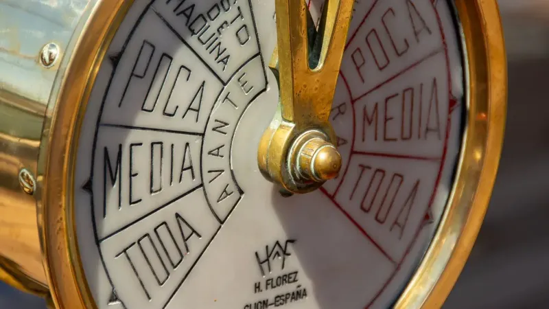 Detailed view of a vintage ship's telegraph dial with Spanish text in sunlight.
