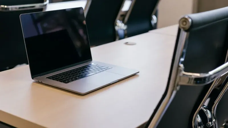Abra la computadora portátil en una mesa de conferencias de madera con elegantes sillas negras en un entorno de oficina moderno.