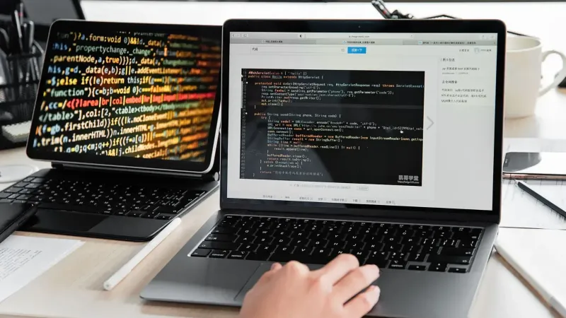 A developer writing code on a laptop, displaying programming scripts in an office environment.