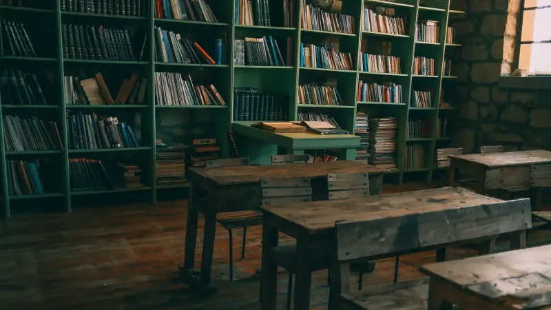A rustic, vintage classroom featuring wooden desks and bookshelves filled with books.
