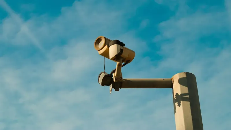 A surveillance camera mounted outdoors against a bright blue sky, symbolizing security and monitoring.