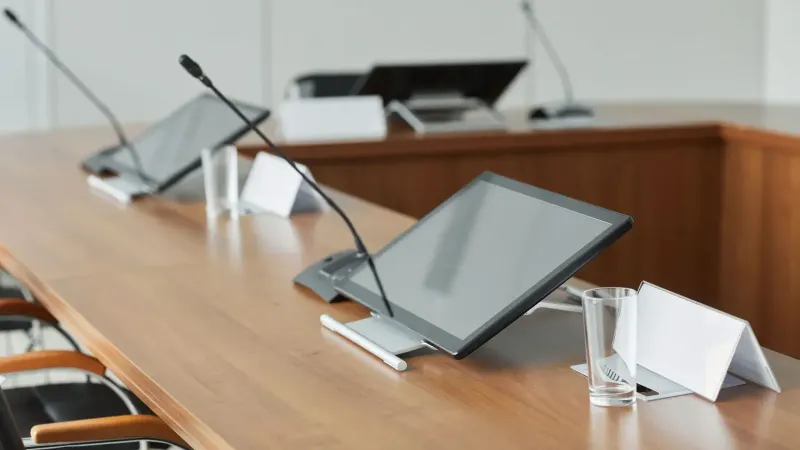 Una moderna sala de conferencias con elegantes monitores y micrófonos sobre una mesa de madera, ideal para reuniones.