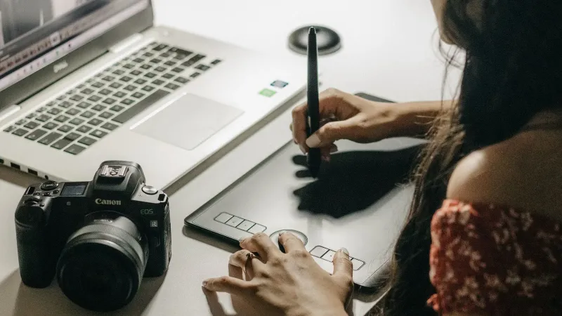 Close-up of a woman using a graphics tablet to create digital art with a laptop.