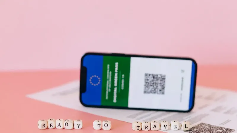 Smartphone que muestra el pase verde digital en una superficie rosa con cuentas de viaje.