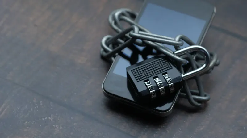 Close-up of a smartphone wrapped in a chain with a padlock, symbolizing strong security.