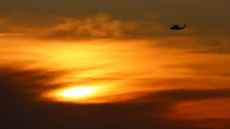 A silhouette of a helicopter flying against a golden sunset sky in Los Angeles.