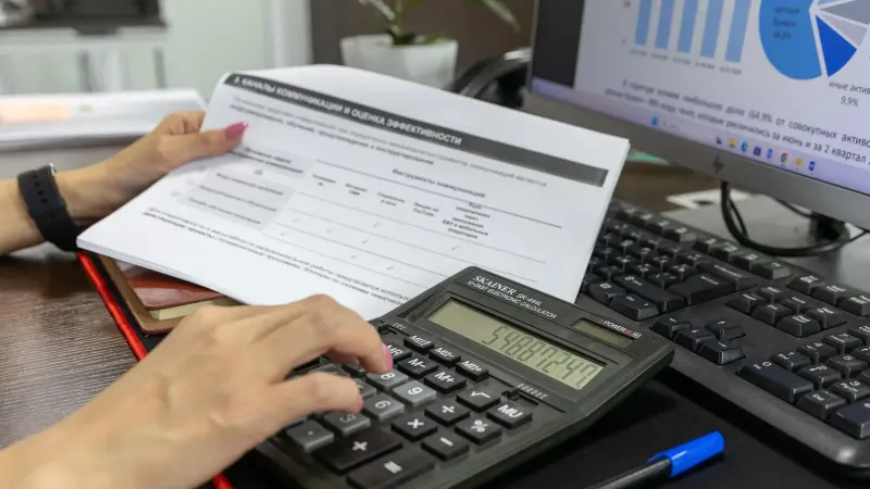 Una persona calcula los datos financieros usando una calculadora y un documento, trabajando en un escritorio de oficina.