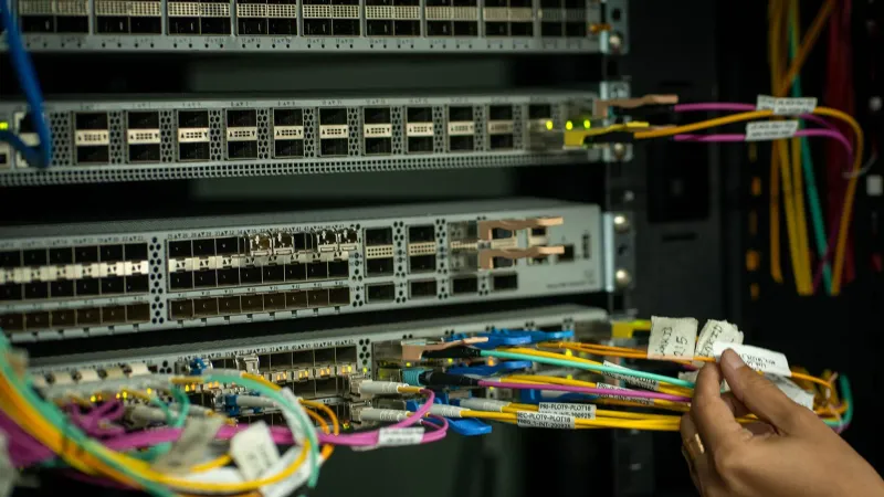 A hand managing fiber optic cables in a server room, showcasing modern connectivity.