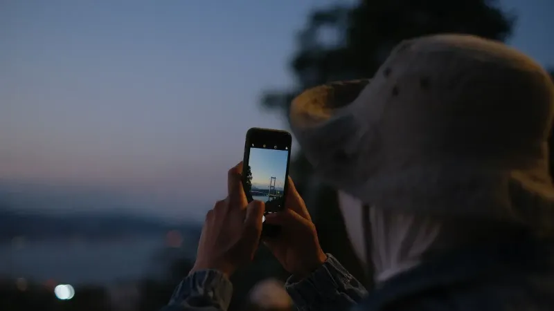 Persona tomando una foto del puente del Bósforo en Estambul al anochecer usando un smartphone.