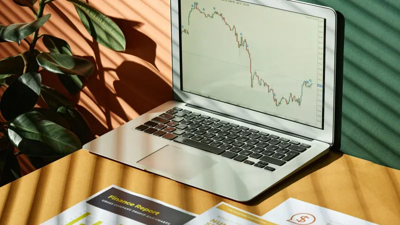 Laptop displaying a financial graph with reports, in a sunlit workspace.