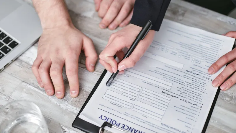 Close-up image of two people signing an insurance policy document on a wooden desk.